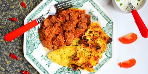 Homemade beef bhuna curry with naan bread and raita